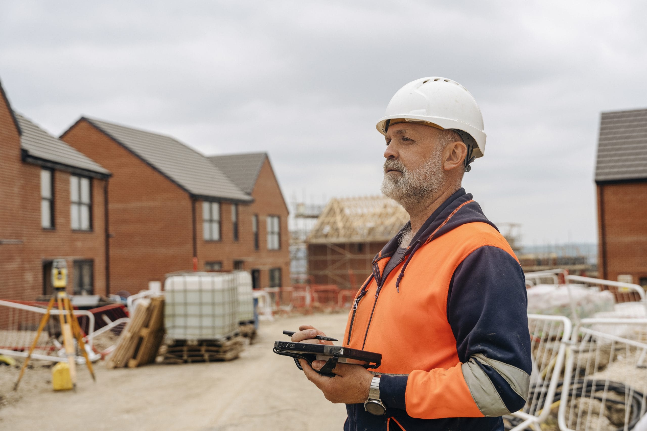 Construction Site Manager wearing hard hat and high-vis vest carrying out quality inspection on a residential housing development construction site.