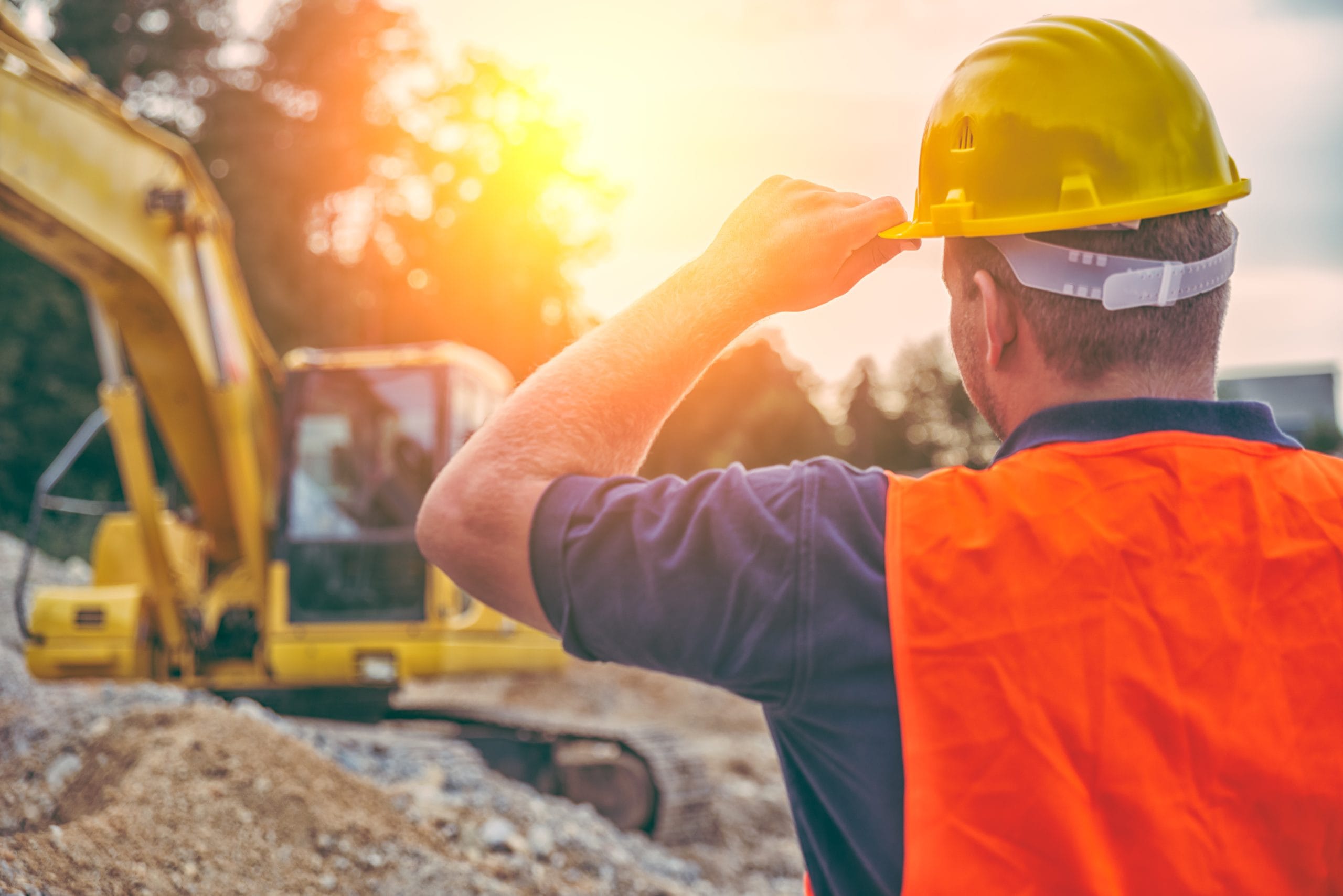 Construction worker in hard hat and high-vis vest marshalling plant machinery (excavator)
